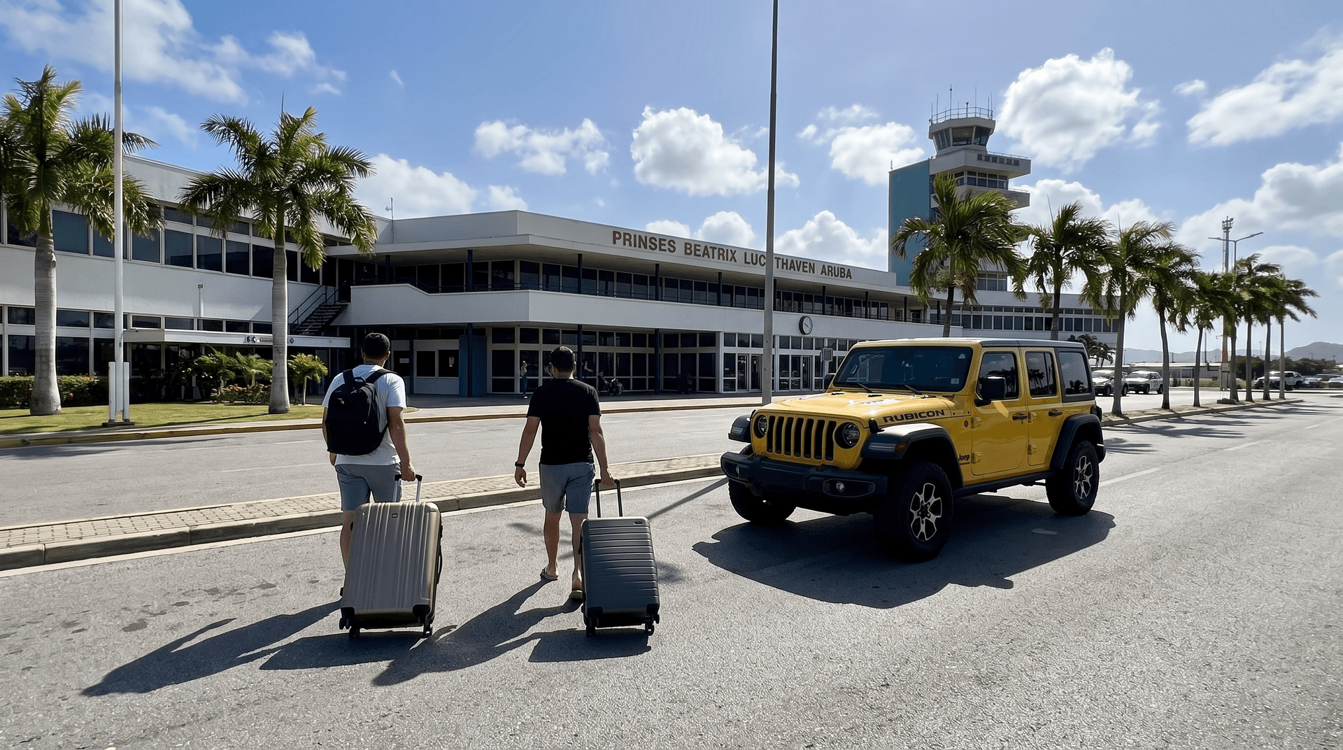 Two travelers pull suitcases toward a yellow Jeep outside the arrivals area at Queen Beatrix International Airport