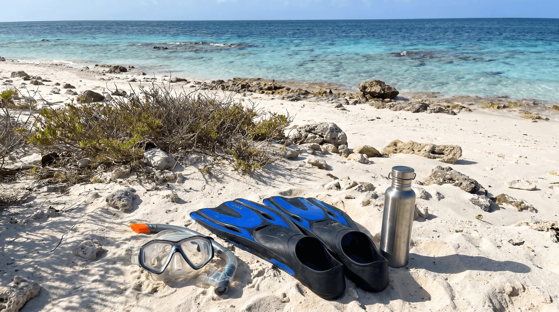 Snorkel mask, fins and a water bottle on the white sand of No Name Beach on Klein Bonaire