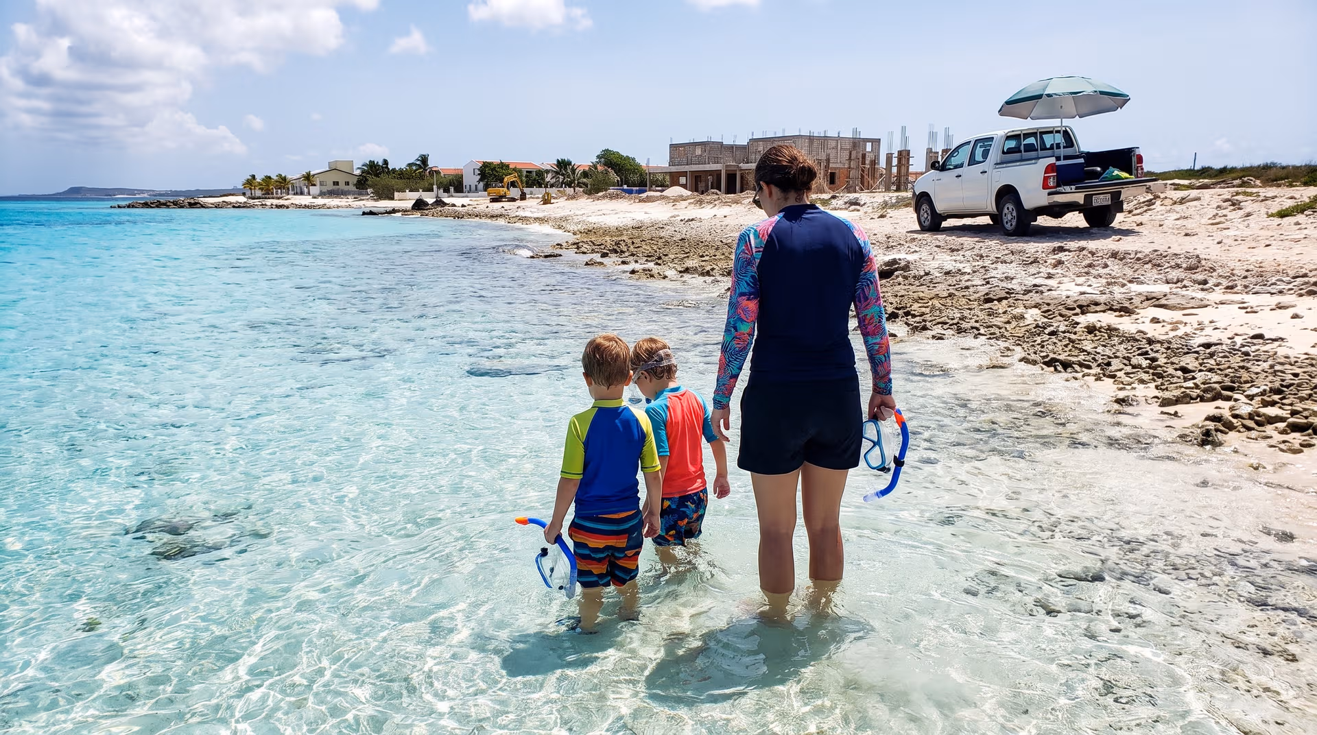 Gezin met snorkelmaskers in ondiep helder water bij een pick-up op Bonaire