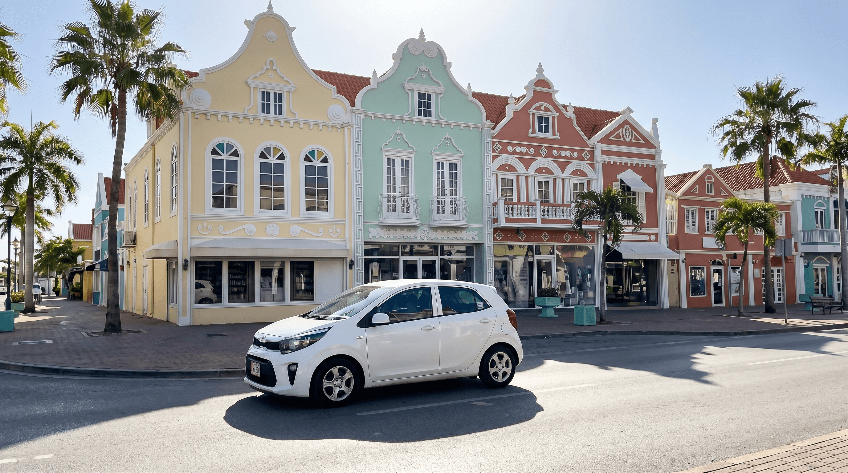 Witte huurauto rijdt door een straat met pastelkleurige koloniale gevels in Oranjestad op Aruba