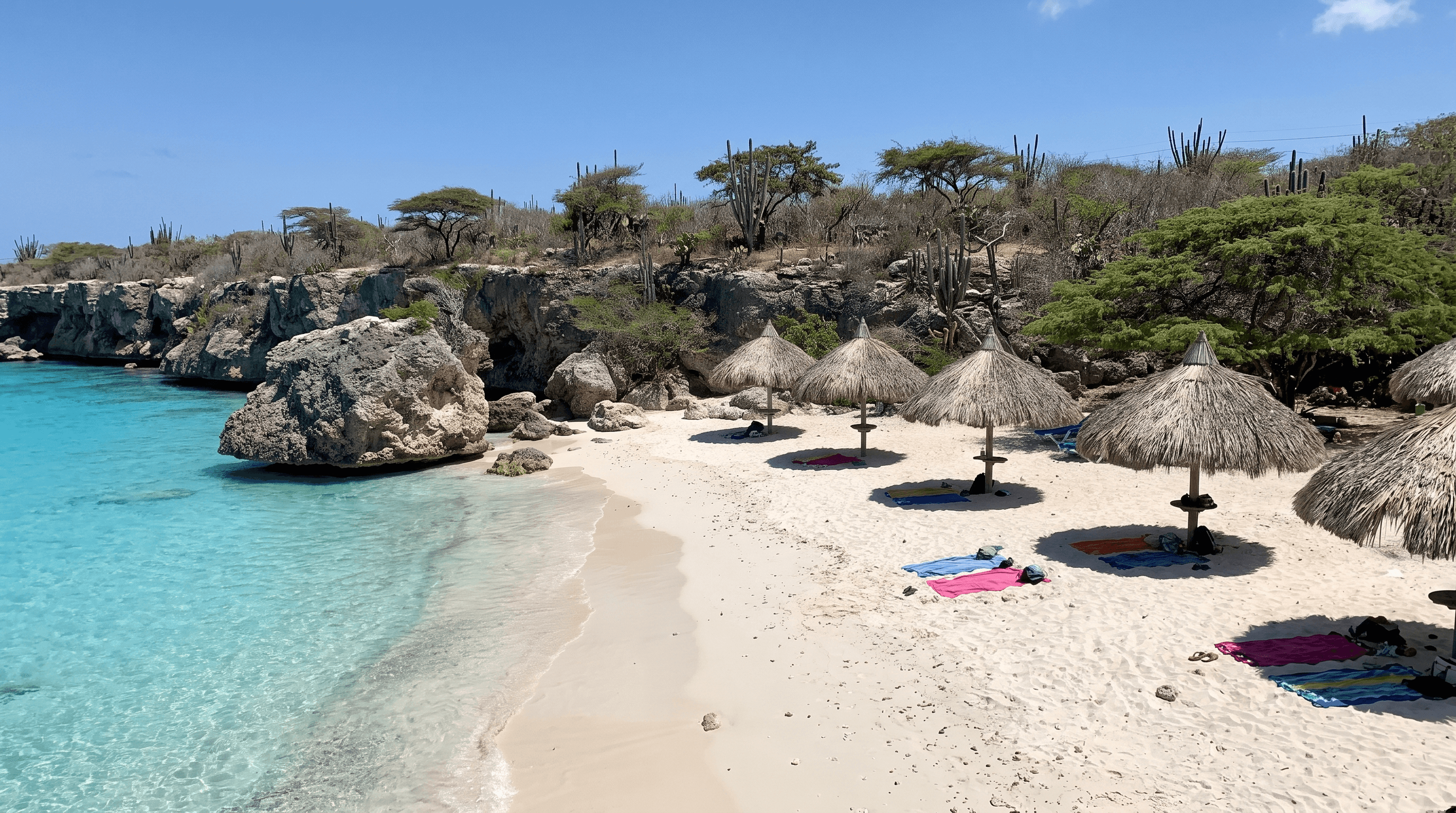Rustig strand met turquoise water en palapa parasols aan de westkust van Curaçao in oktober