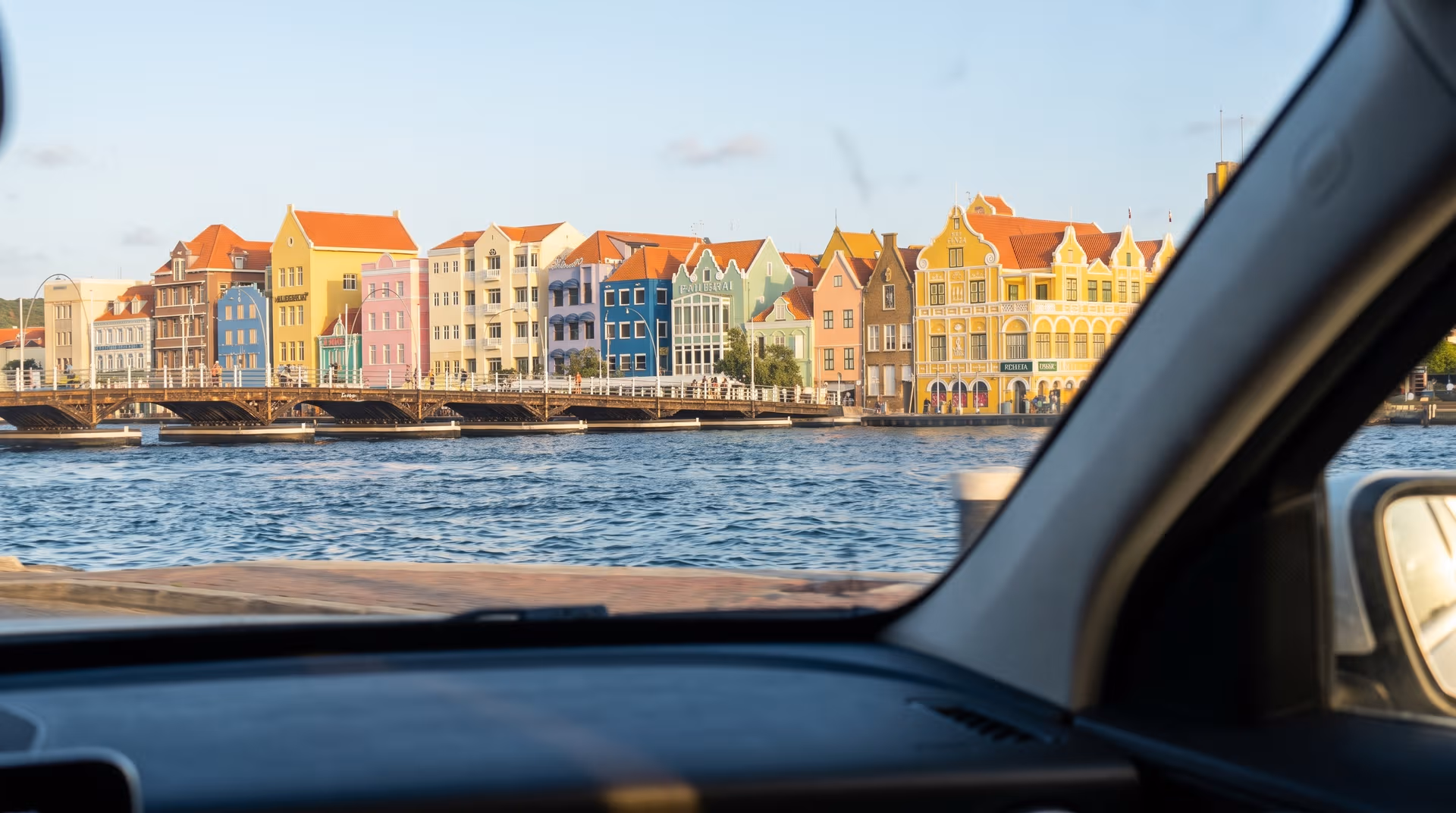 Uitzicht vanuit een huurauto op de gekleurde panden van de Handelskade in Willemstad
