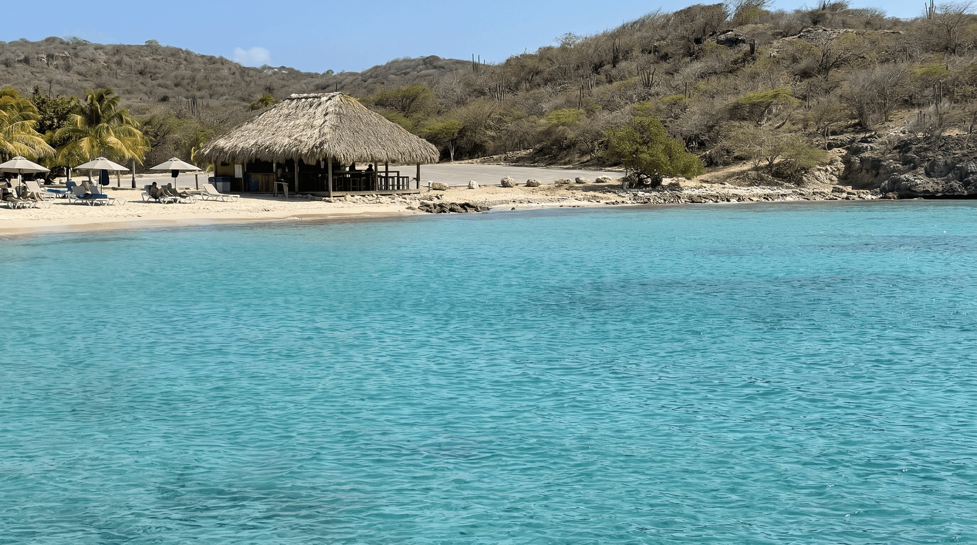 Calm turquoise bay and palm-thatched beach bar at Jan Thiel beach in Curaçao on a sunny day