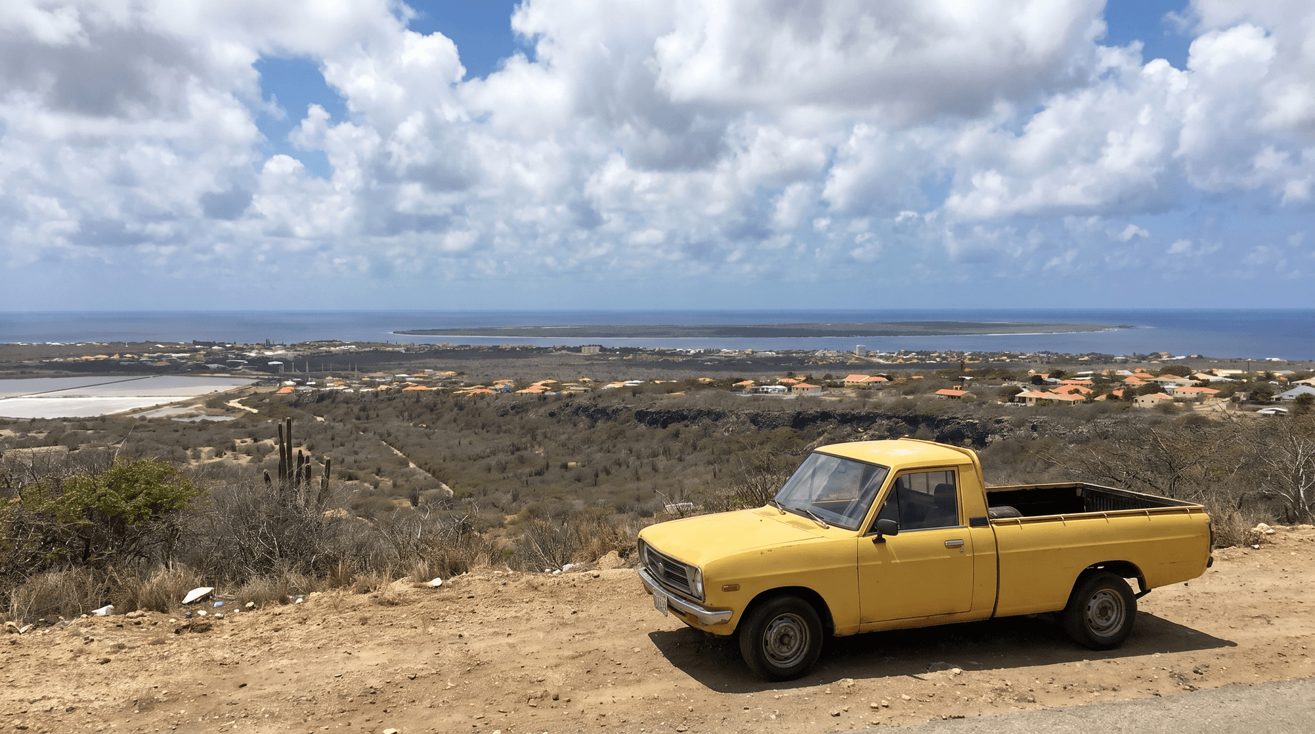 Gele pick-up langs de kustweg van Bonaire met uitzicht op Kralendijk en de zee