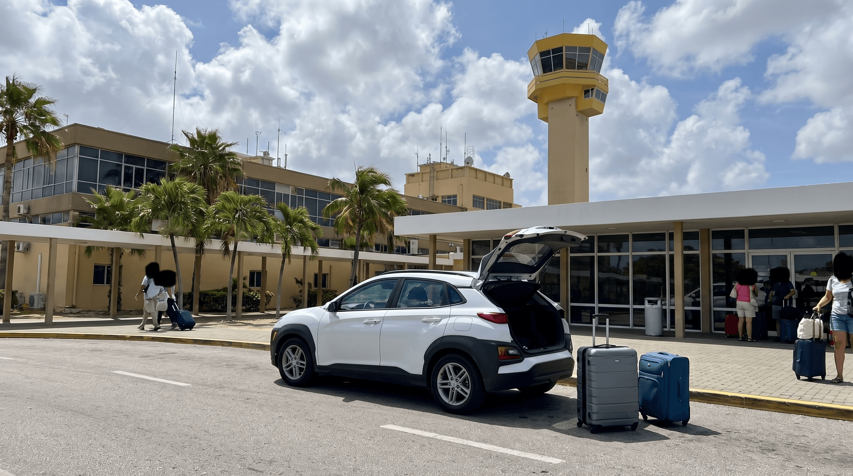 Witte huurauto met open kofferbak bij de aankomsthal van Curaçao International Airport