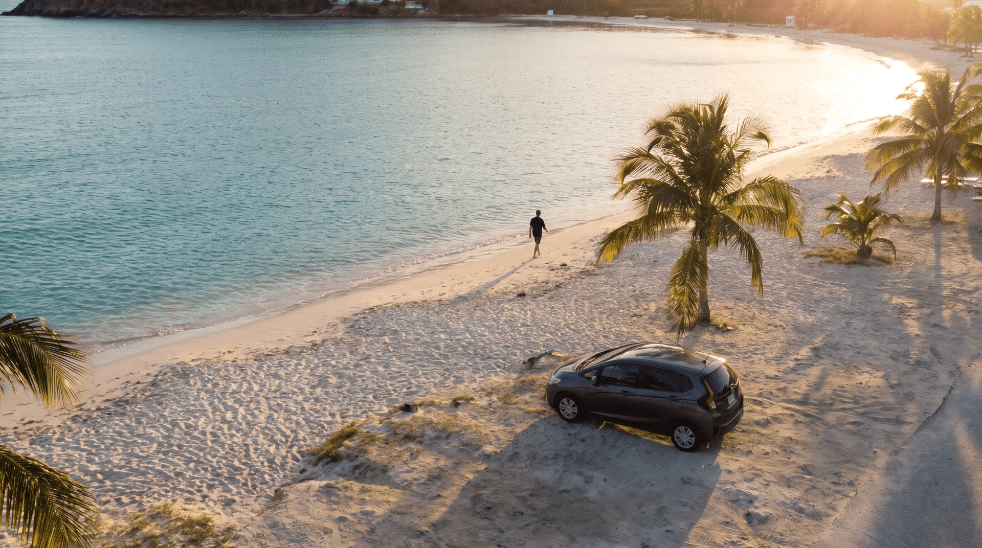 Kleine grijze auto geparkeerd op een zandterrein aan een rustige baai op Sint Maarten bij zonsondergang