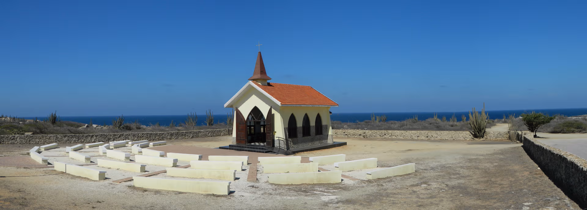 Alto Vista Chapel on Aruba, a yellow chapel with a red roof against a deep blue sky