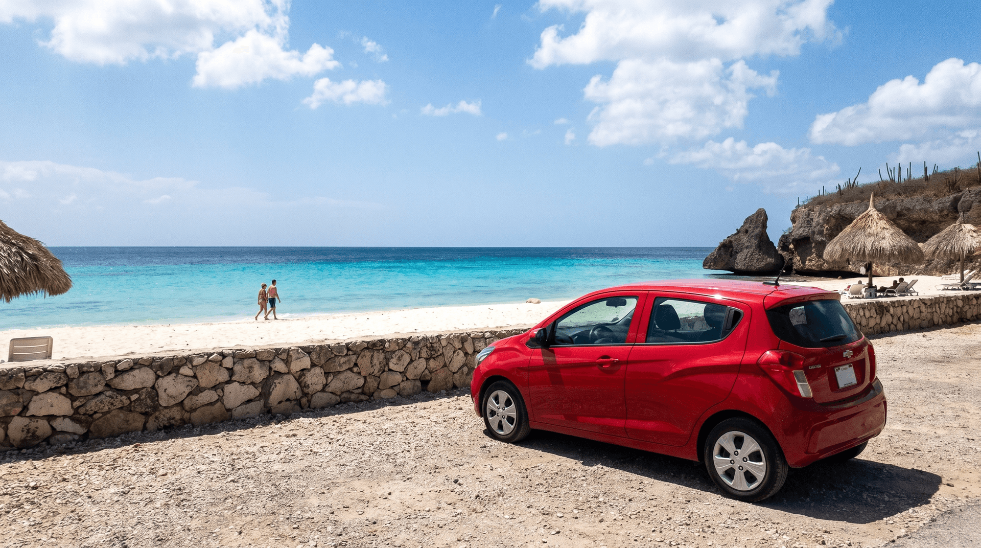 Kompakter roter Mietwagen parkt oberhalb des Strandes Cas Abao auf Curaçao mit türkisfarbenem Wasser im Hintergrund