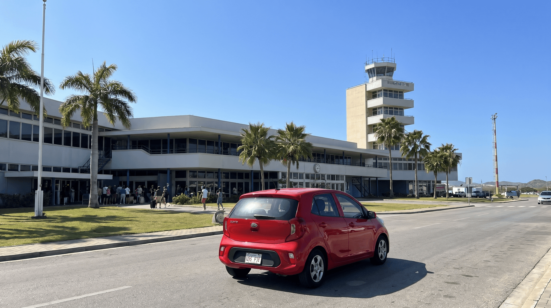 A red compact rental car leaving Queen Beatrix International Airport in Aruba