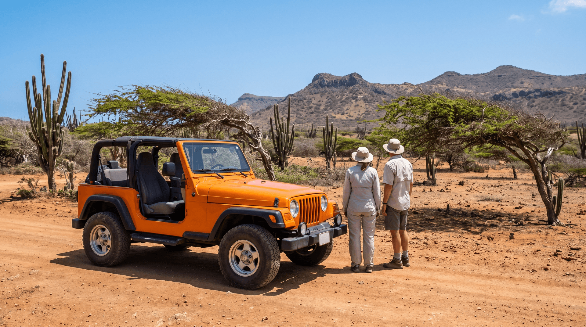 Orange 4x4 jeep parked on a red dirt trail in Arikok National Park, Aruba, with two travelers admiring the view