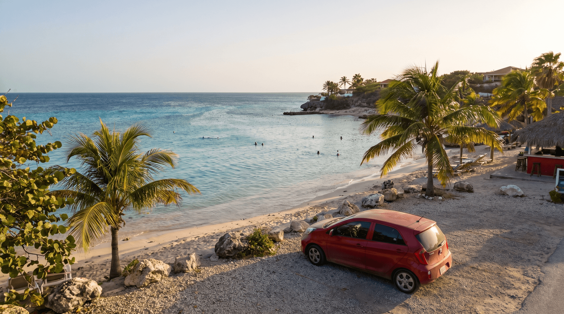 Rood compact huurautootje geparkeerd aan de rand van Jan Thiel beach op Curaçao bij zonsondergang